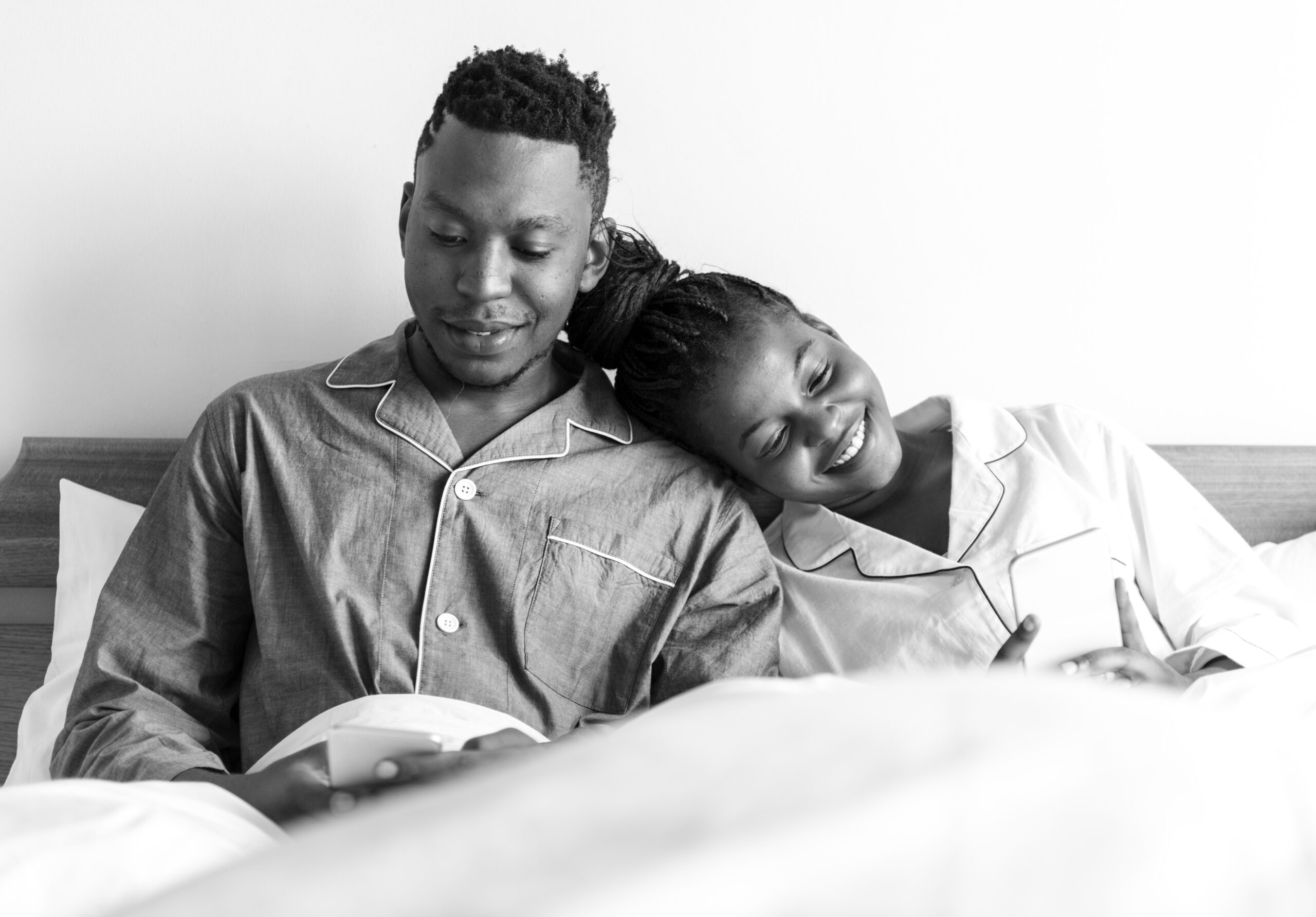 a happy couple using mobile phones in bed